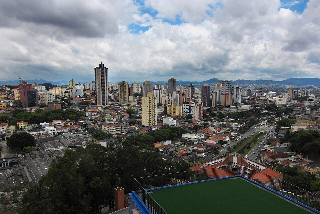 Vista de Osasco com prédios residenciais, casas e avenida arborizada sob céu com nuvens